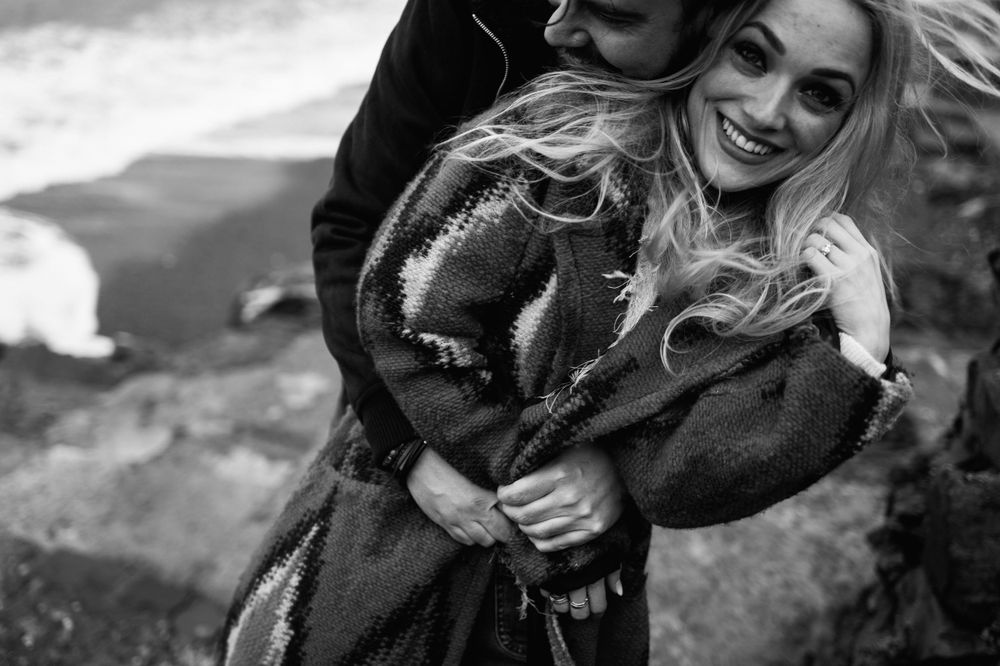 A tender embrace captured in black and white on a windswept coastal cliff.