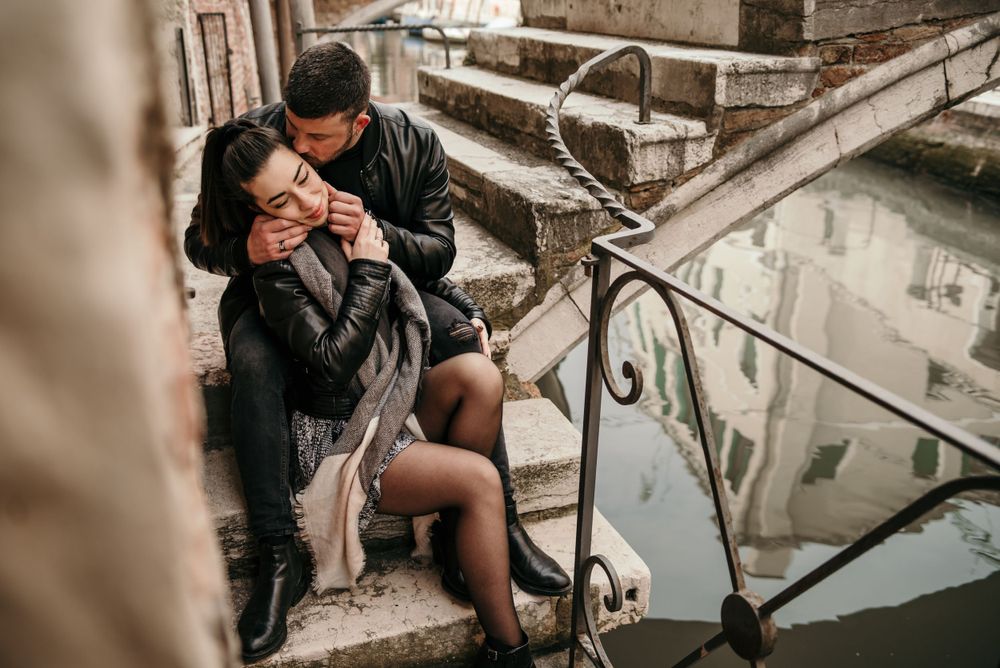 Romantic couple sharing an intimate moment on stone steps near a canal in Venice.