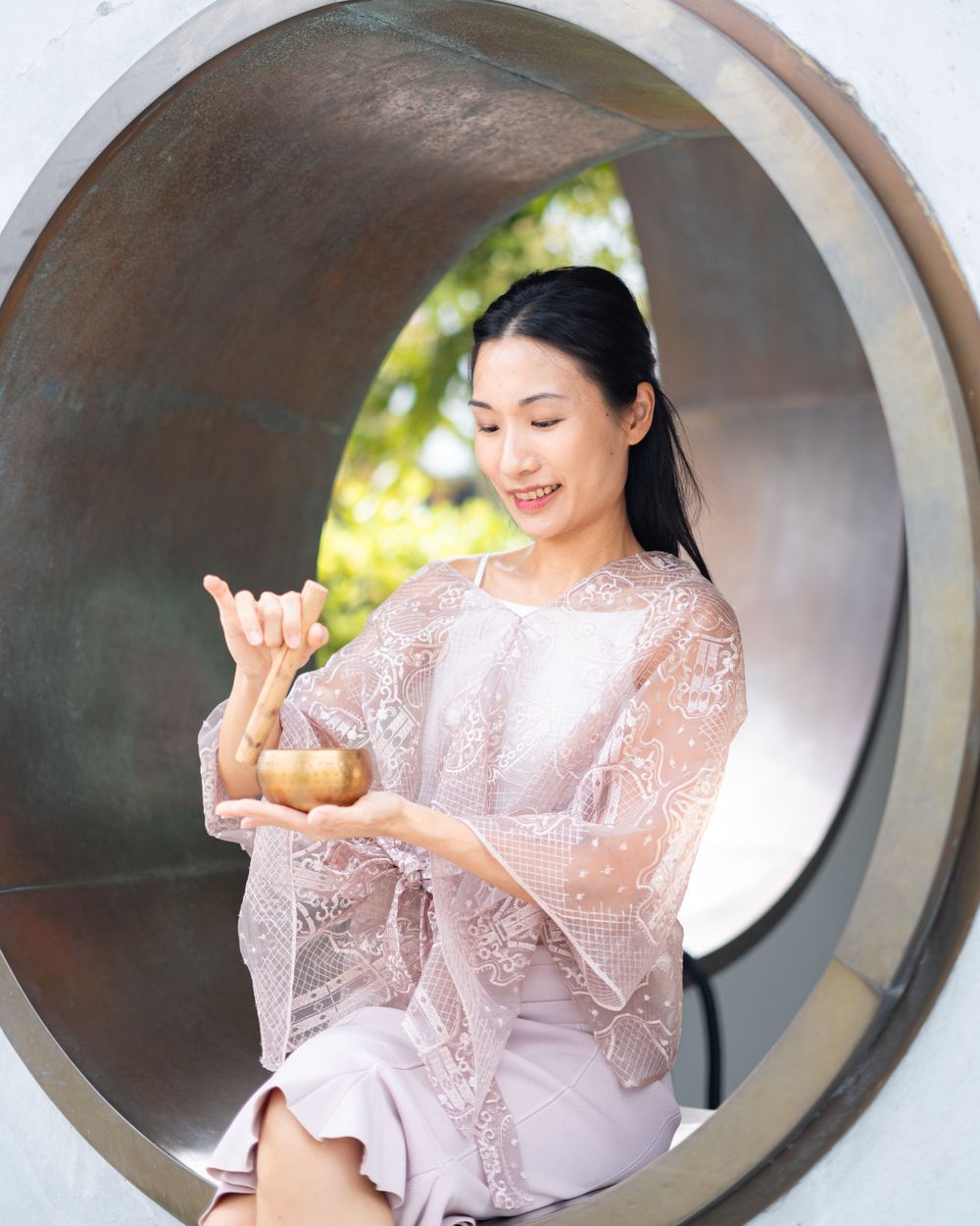 Elegant pose through circular window frame while holding small object in pink lace ensemble.