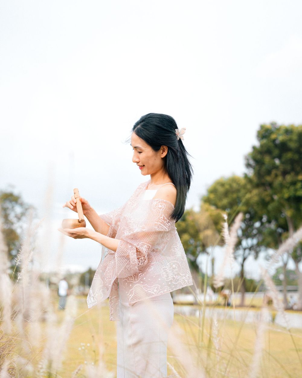Figure in flowing pink dress standing in sunlit field of tall grass.