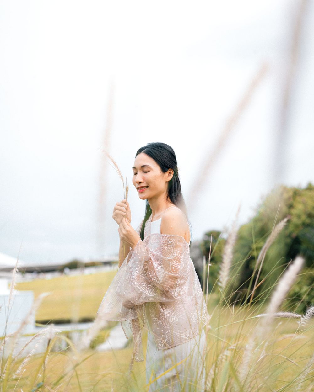 Person in lace dress standing among tall grass holds dried plant stalk.