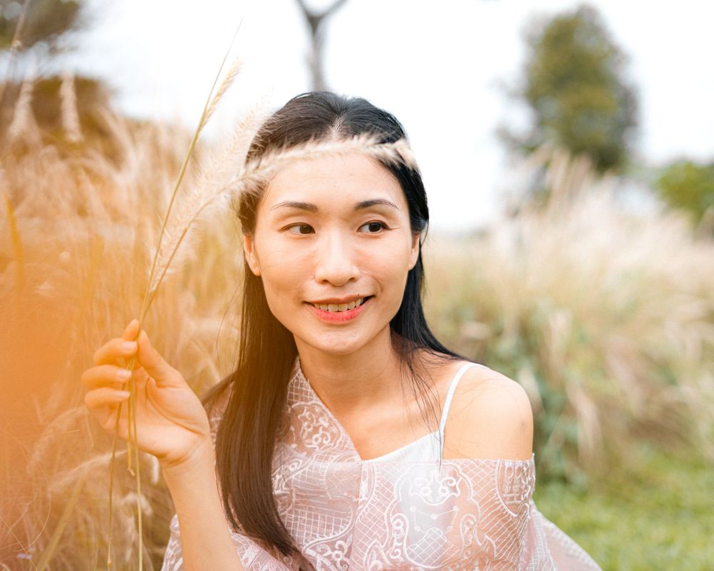 Person in pink dress poses among tall grass with warm lighting.