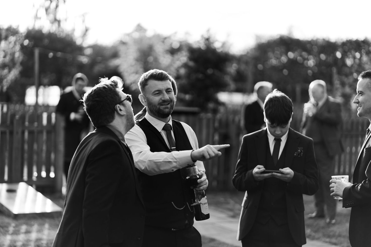Black and white photo showing happy wedding guests laughing and enjoying a reception in an outdoor garden setting.