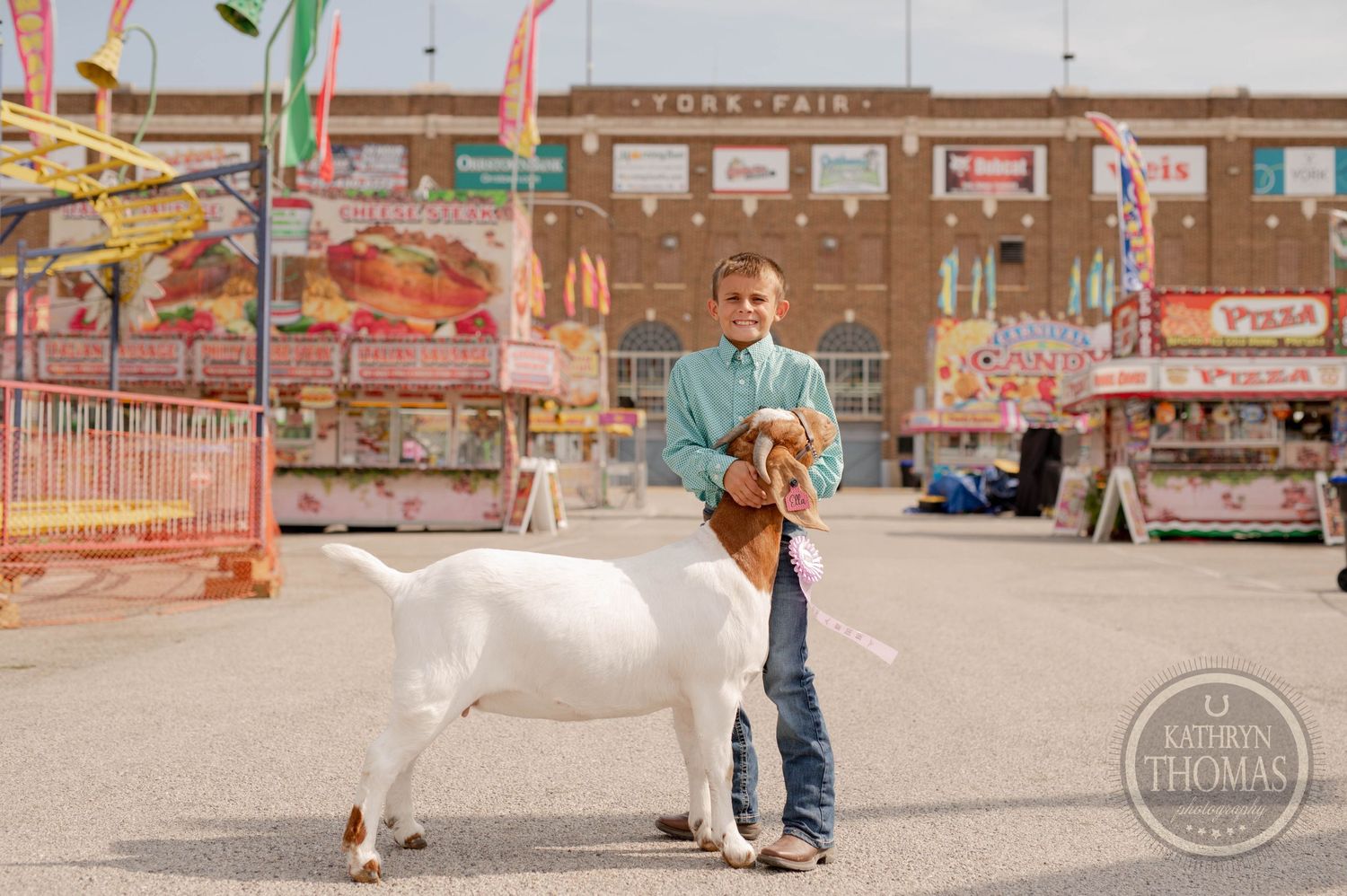 Young exhibitor shows a white goat at state fair with carnival rides in background.