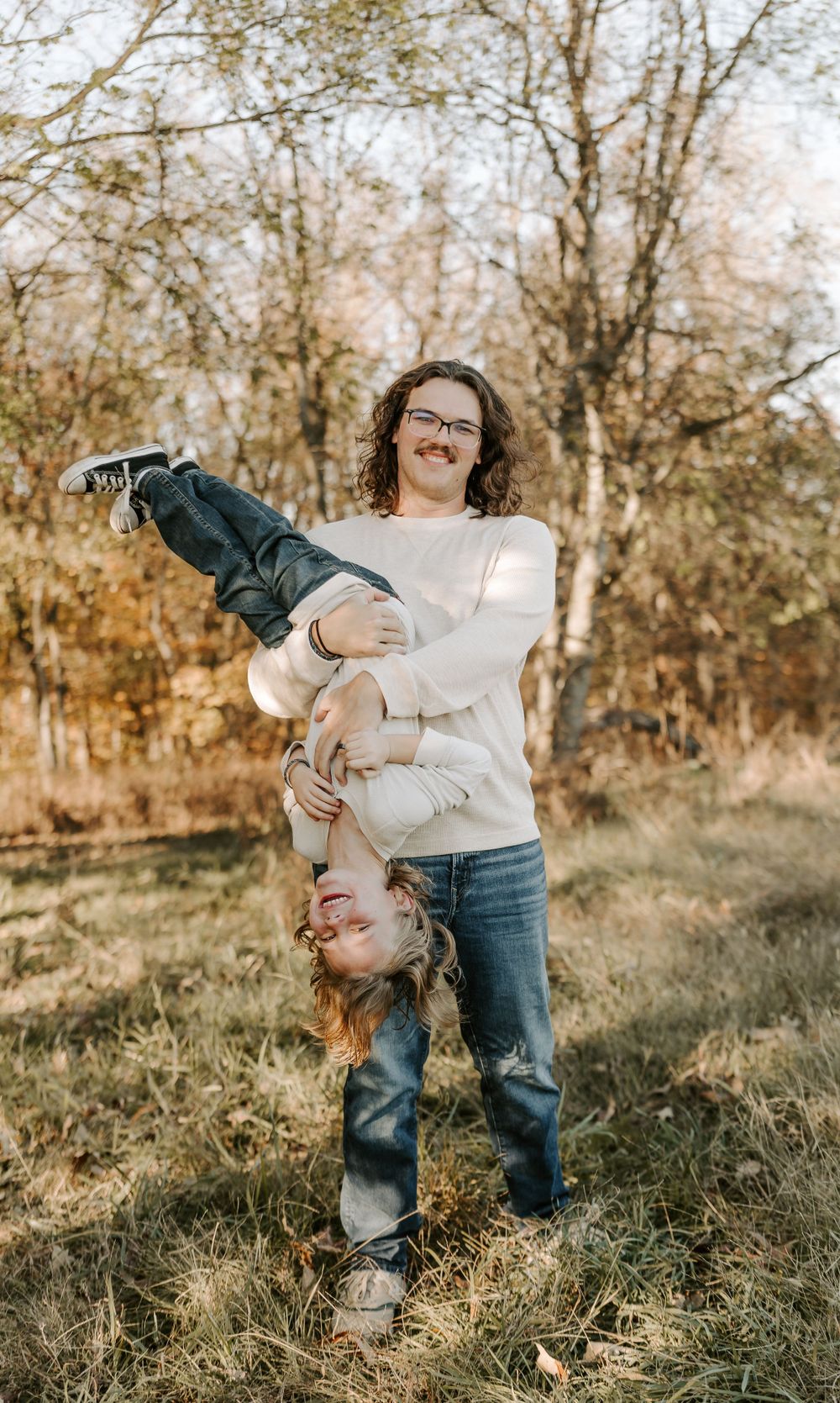 Playful family interaction with child being swung upside down in grassy field.