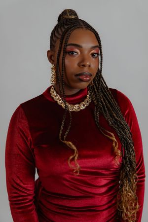 Studio portrait featuring red velvet dress, braided hairstyle, and gold statement necklace.