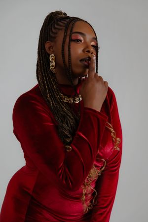 Stylish portrait showcasing red velvet dress, intricate braids and gold accessories.
