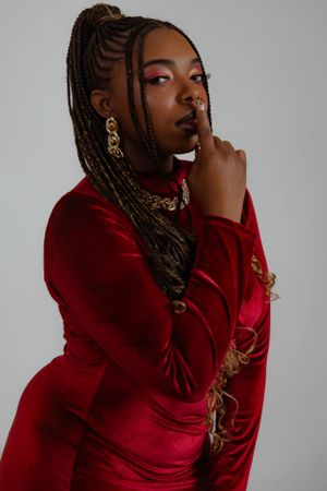 Fashion model in red velvet dress poses with dramatic makeup and ornate gold jewelry.