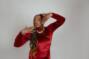 Model in red velvet dress strikes dynamic pose with hands framing face.