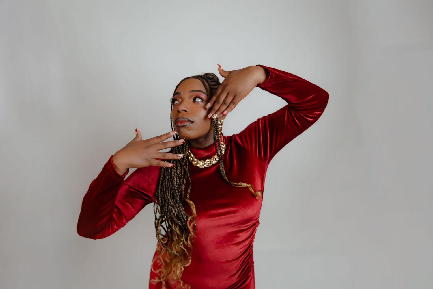 Fashion model in red dress poses expressively with hands near face in studio setting.