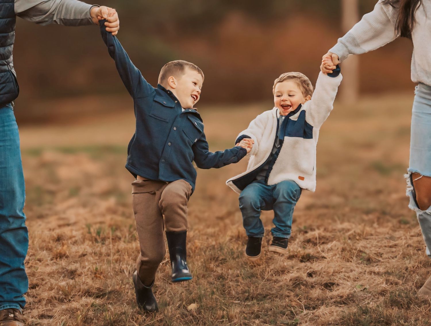 Siblings laughing together being lifted by their parents in Maine