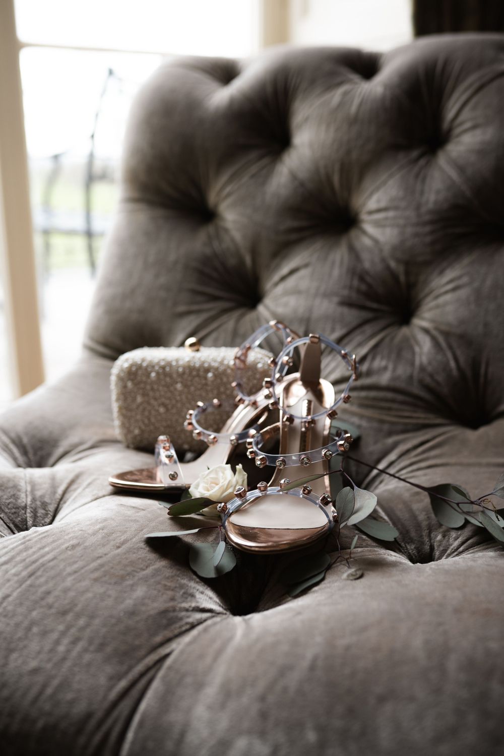 Wedding shoes with crystal details resting on tufted grey velvet couch.