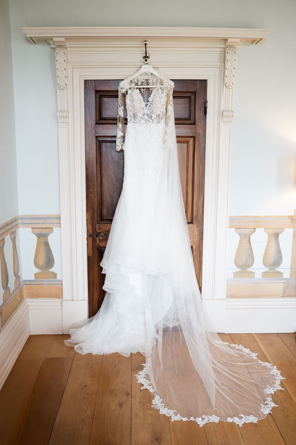 White lace wedding gown hanging against wooden paneled wall in elegant venue.