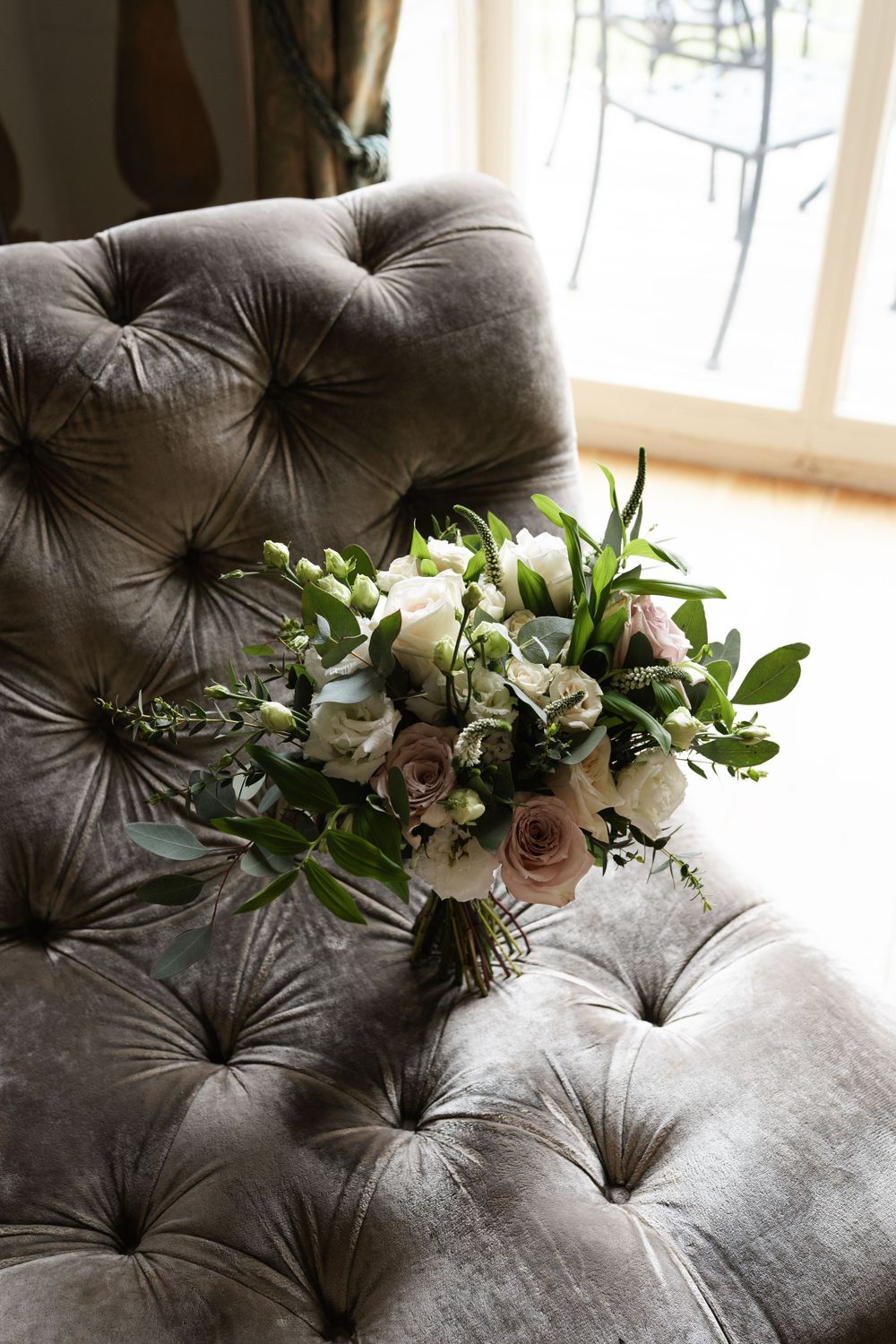 Fresh white and blush floral arrangement displayed on grey tufted velvet sofa.