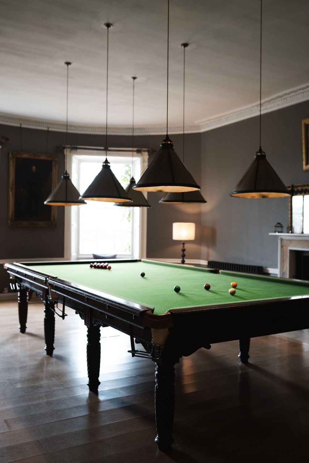 Room with multiple snooker tables under modern pendant lighting.