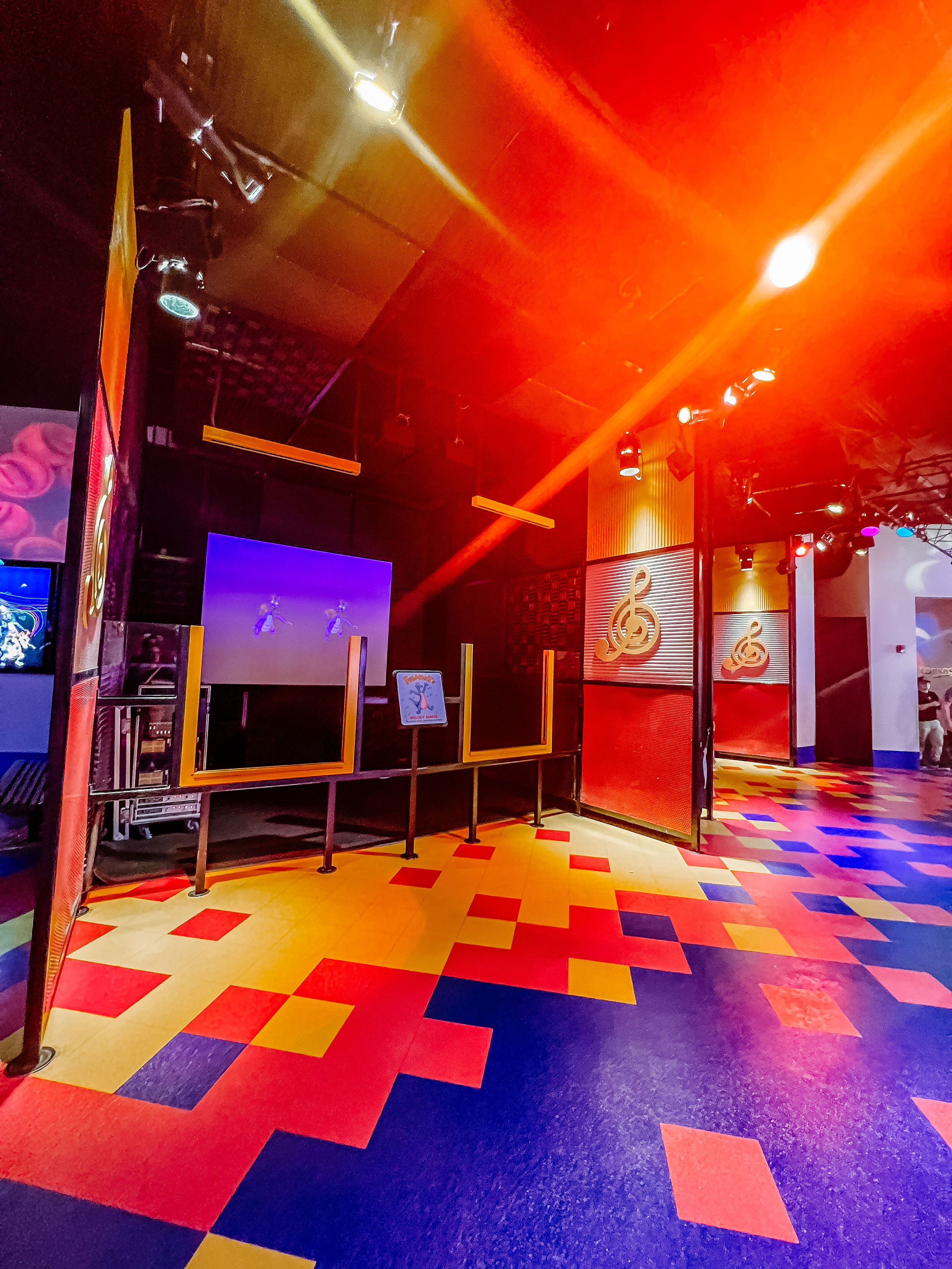 A modern dance studio with vibrant red lighting and colorful geometric floor tiles creates an energetic atmosphere.