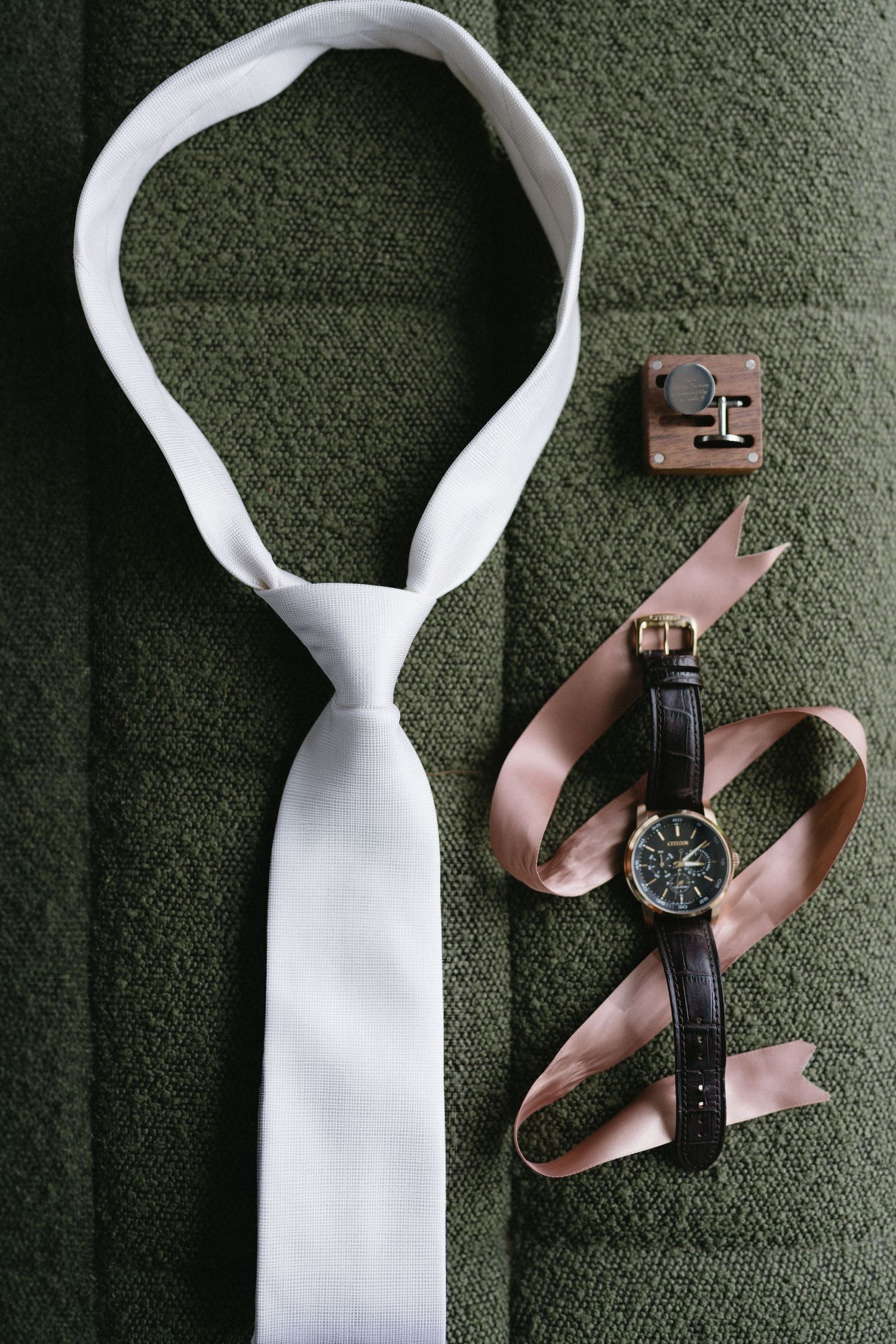 White tie and vintage wristwatch with leather strap arranged on green textile surface.