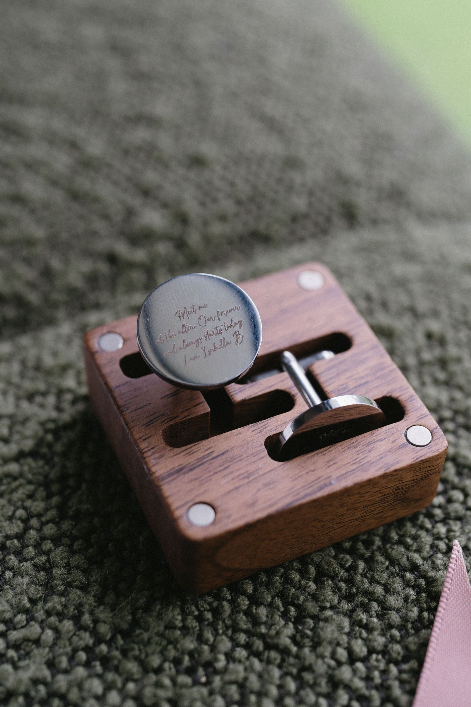 Wooden box with engraved cufflinks on dark green textured fabric.
