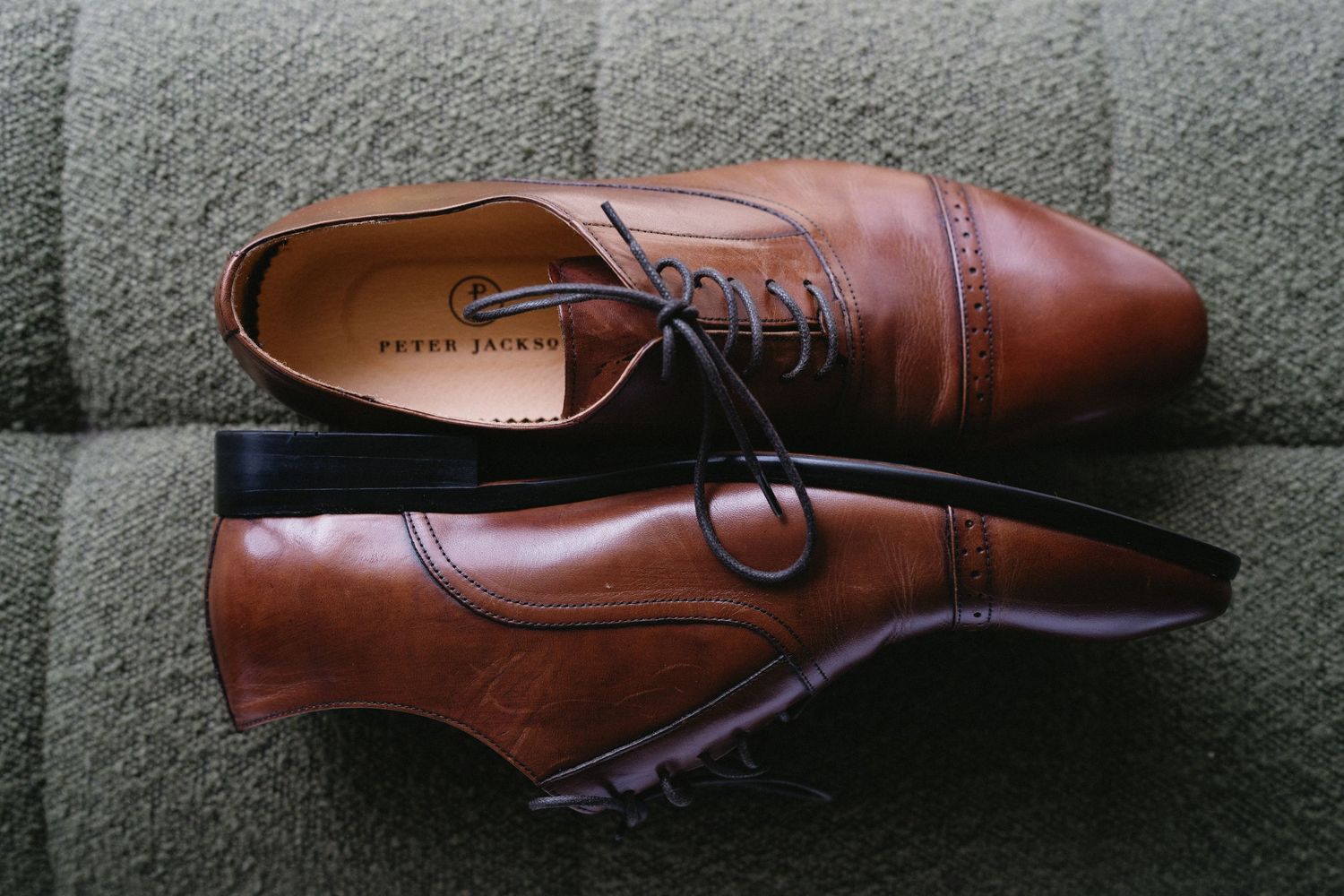 Classic brown leather oxford dress shoes on gray textile surface.