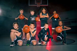 Youth basketball team poses with basketballs on a dark court with dramatic lighting effects in the background.