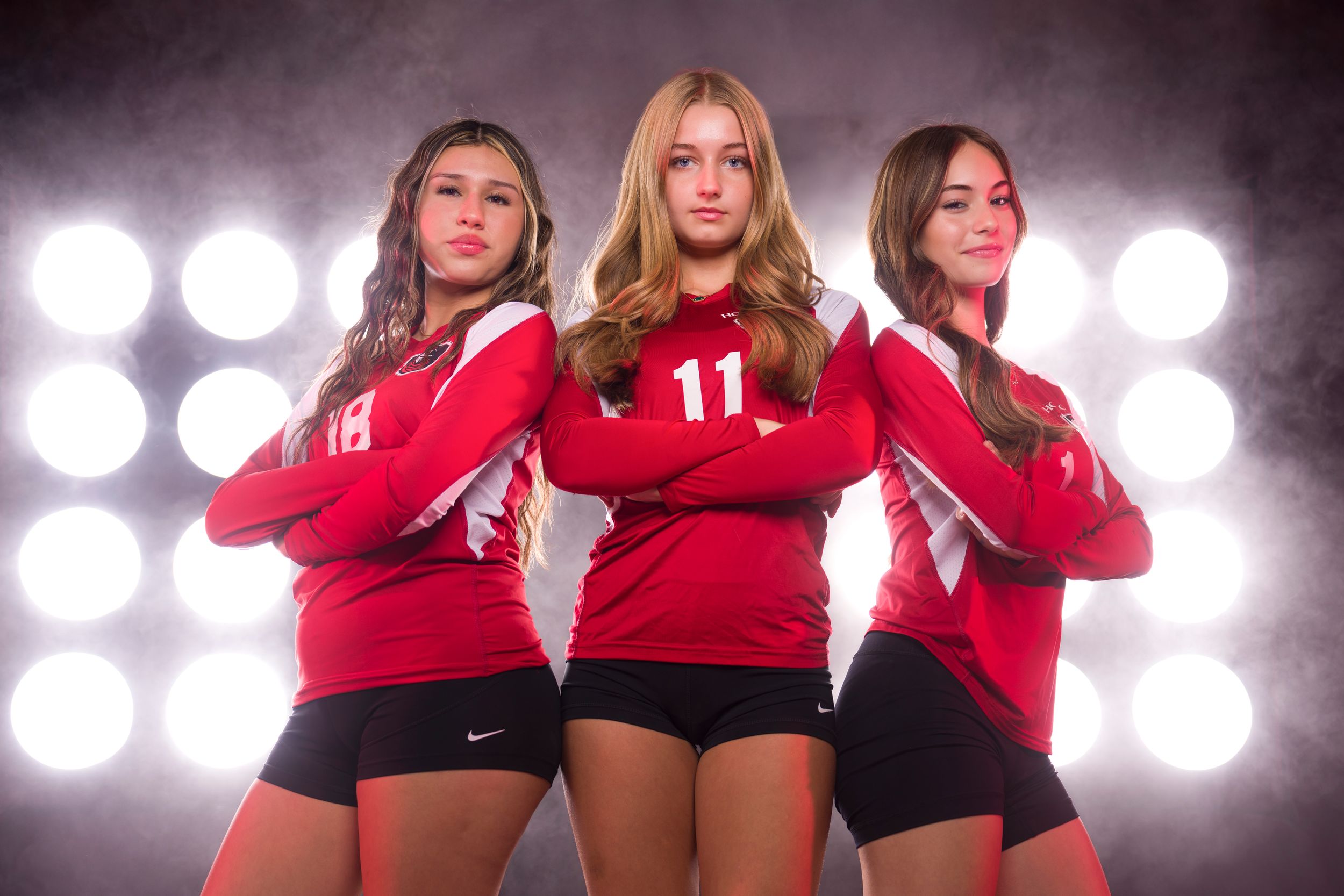 Three athletes pose in red jerseys and black shorts against dramatic stadium lighting backdrop.