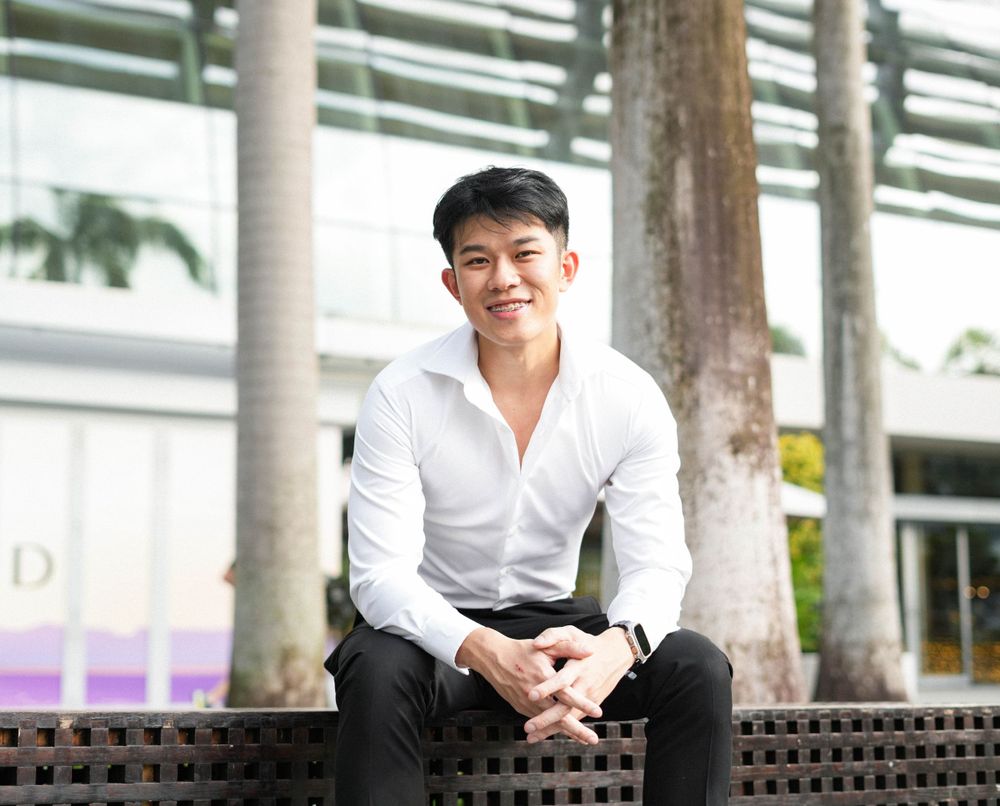 Smiling portrait in white button-down sitting on bench outdoors with palm trees.