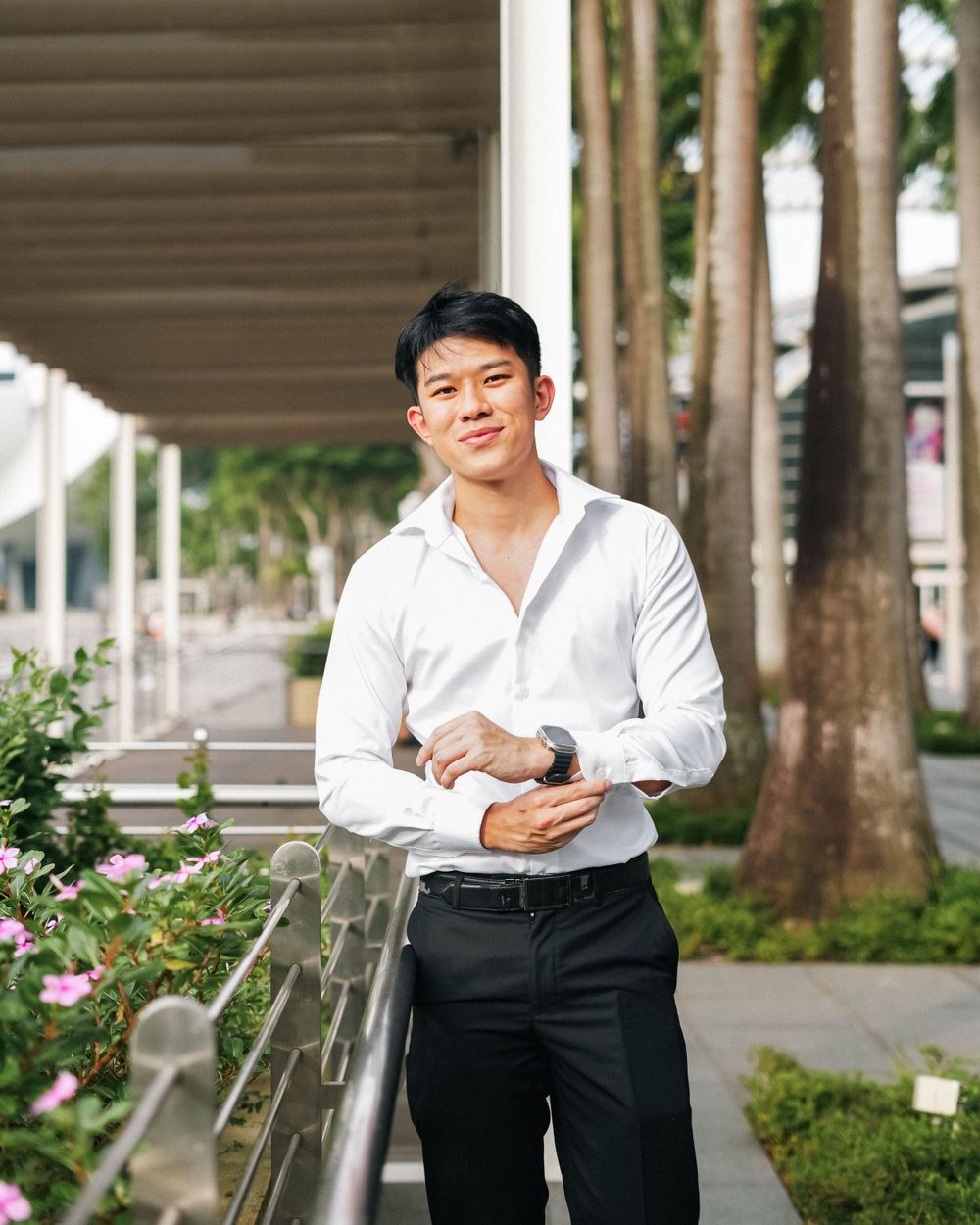 Professional outdoor portrait in white dress shirt and black pants near palm trees and railing.