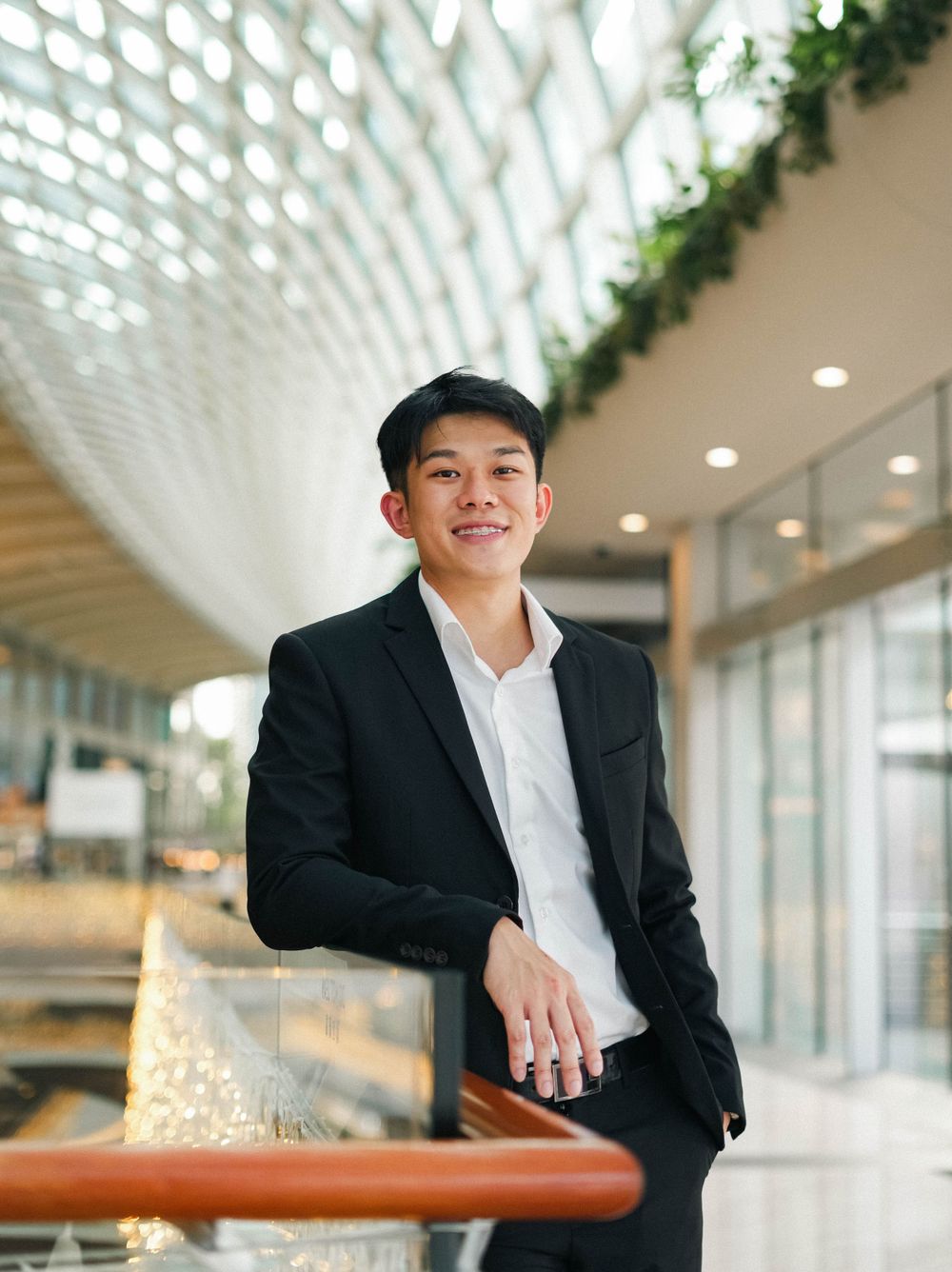 Professional portrait in black suit and white shirt under modern architectural ceiling.