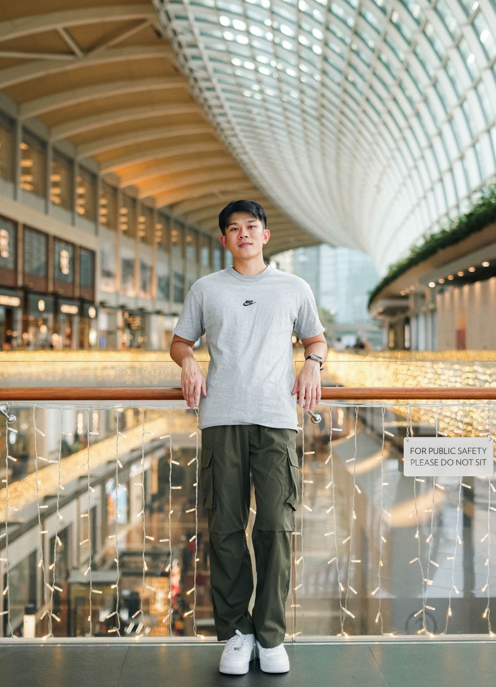 Portrait in grey t-shirt and cargo pants against modern mall interior with curved ceiling.