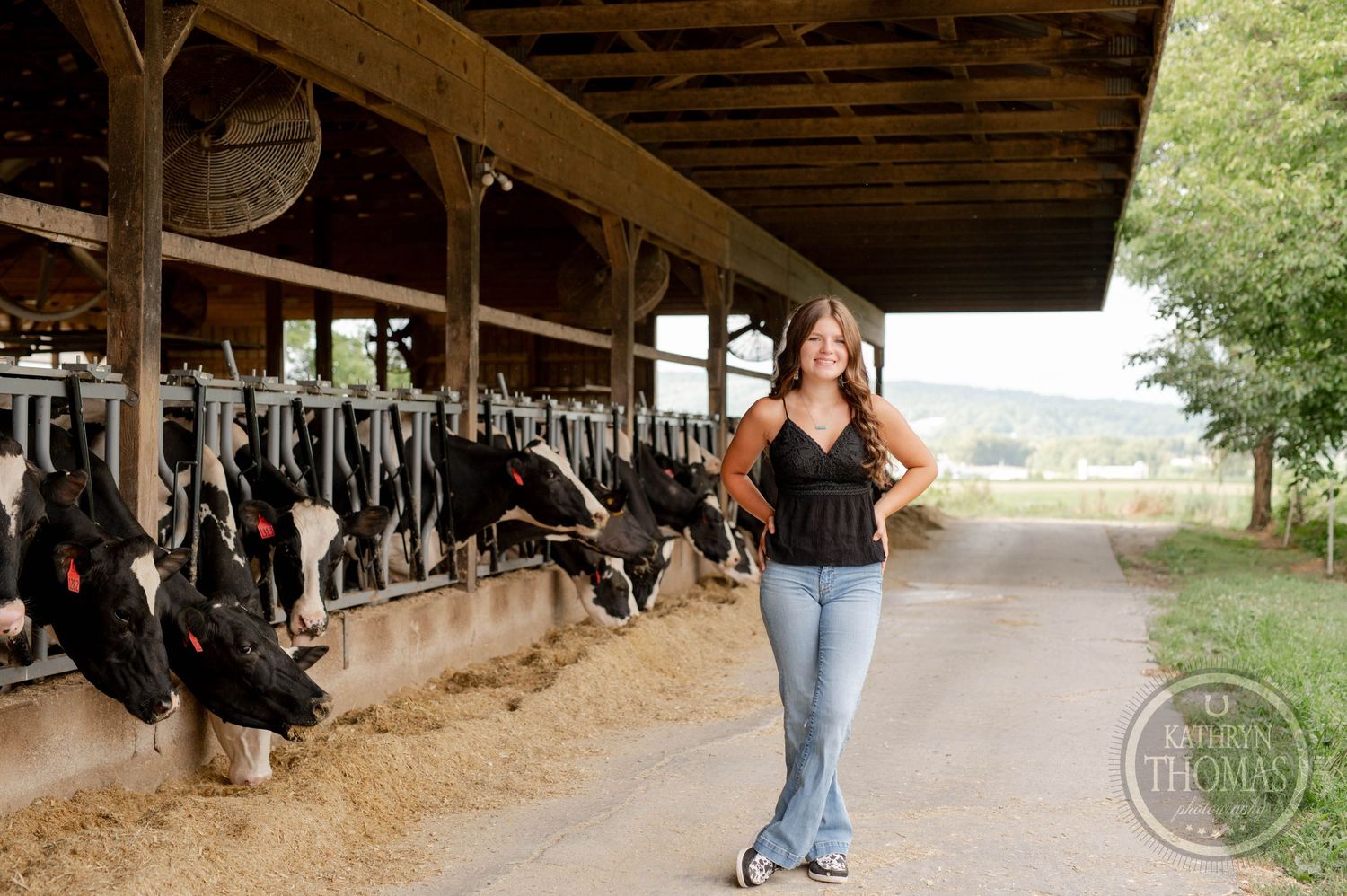 Farm lifestyle portrait with someone in black top and jeans near dairy cows.