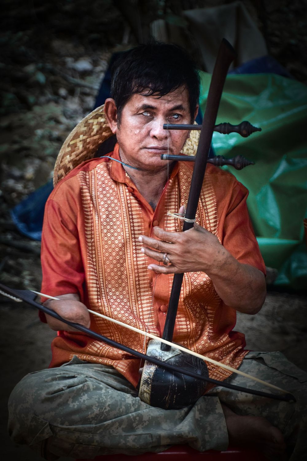Traditional musician holding an ethnic stringed instrument while seated on the ground.