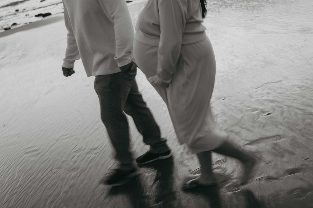 Two people walking together on wet sand at the beach in black and white.