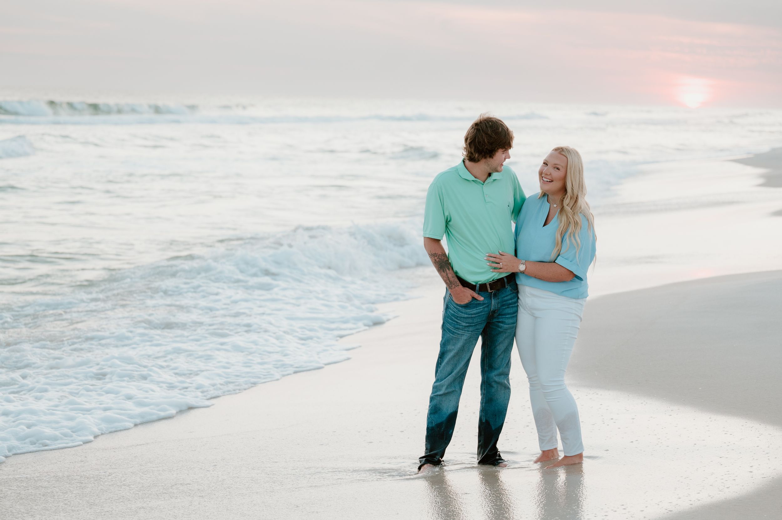 A couple stands together on the shoreline during sunset at Panama City Beach Florida.