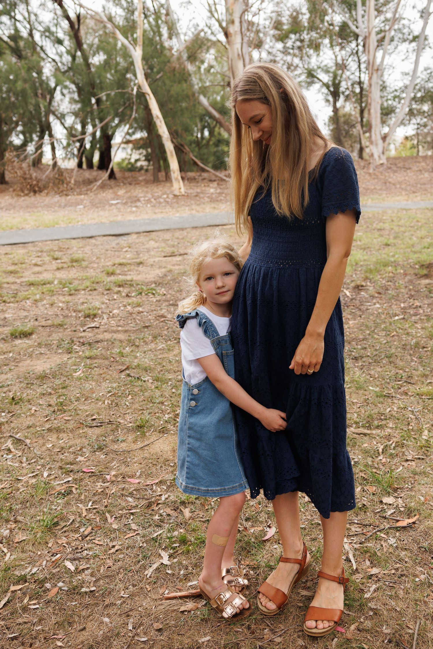 A warm outdoor scene showing a close embrace between two people wearing blue dresses and standing in a wooded area.