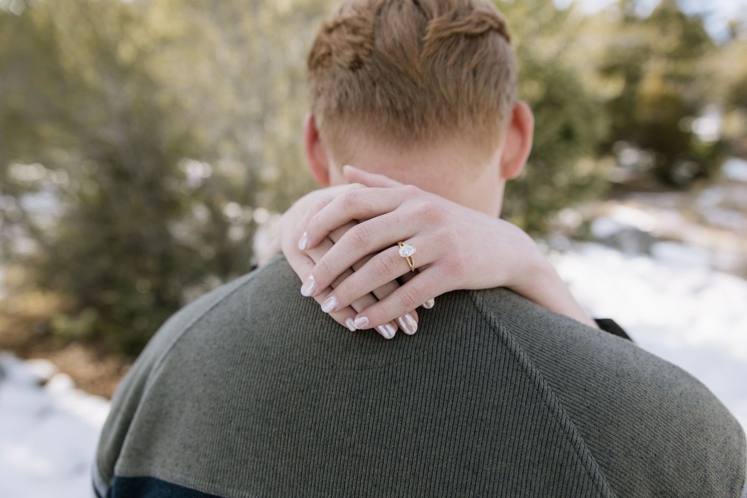 A comforting hand rests on the back of someone wearing a green sweater outdoors in winter.