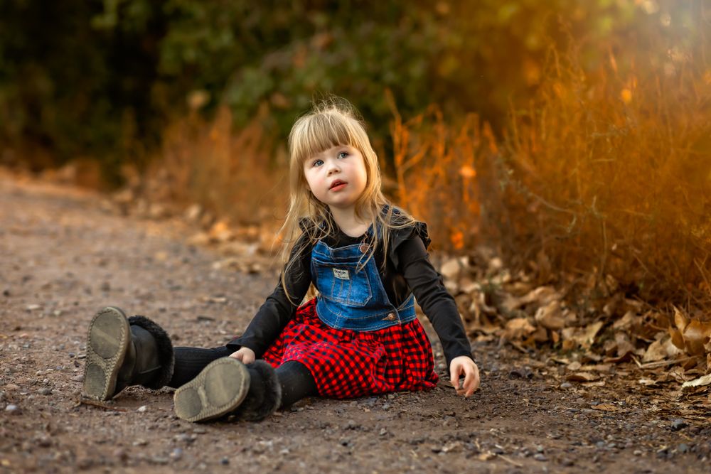 Child in leather jacket and plaid skirt sitting on autumn trail for her family photo session in Queen Creek Arizona