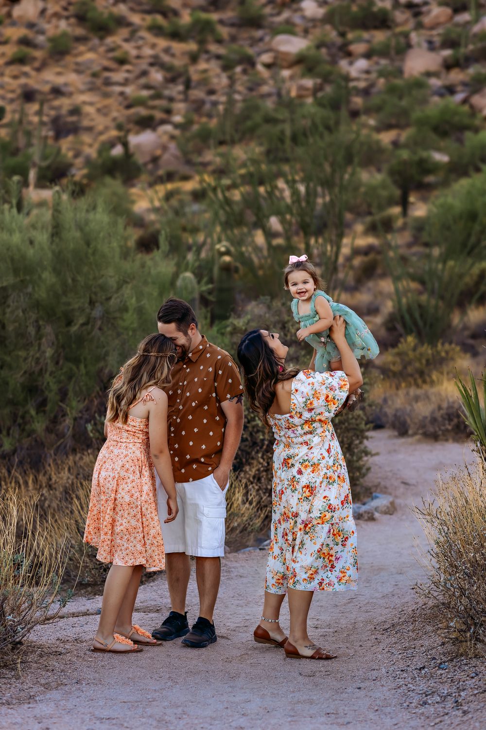 Family in floral dresses and casual wear gathered on desert trail with rocky hills behind them in Scottsdale