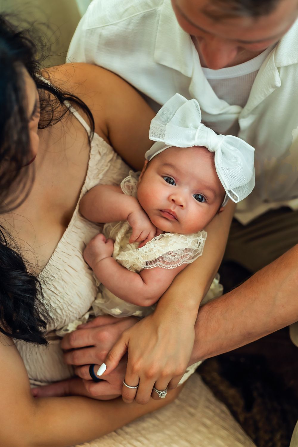 Intimate portrait of a newborn baby wearing white bow headband with parents for their indoor photo session in Goodyear Arizona