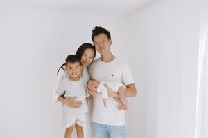 A family wearing white clothing embraces together against a plain white background.