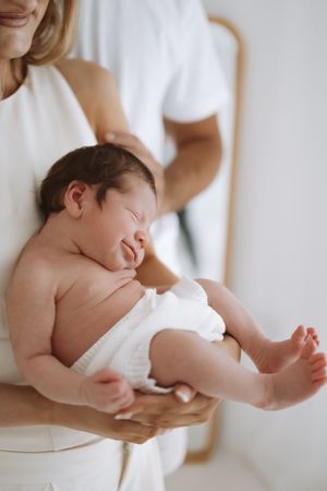 A tender portrait series of a newborn baby cradled in white fabric against a soft neutral background.