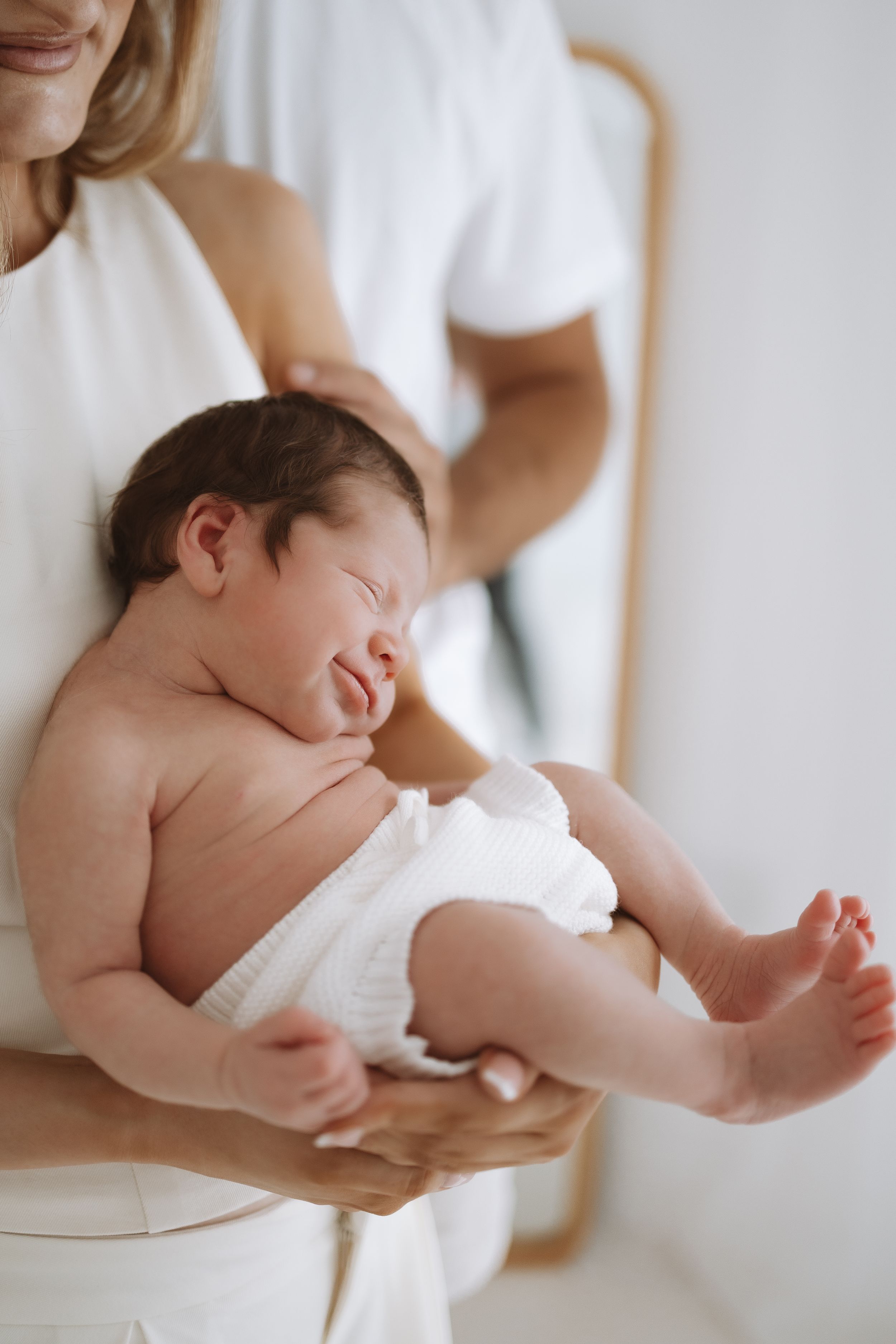 A tender portrait series of a newborn baby cradled in white fabric against a soft neutral background.