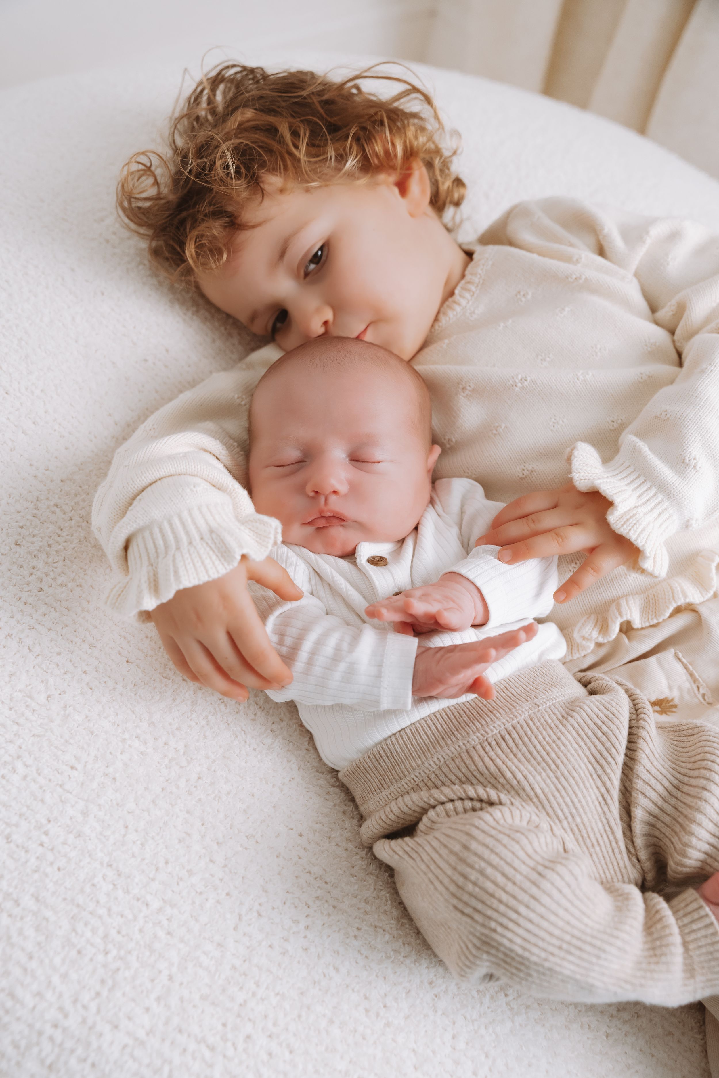 A sleeping baby in a cozy beige knit sweater lies peacefully on white bedding.