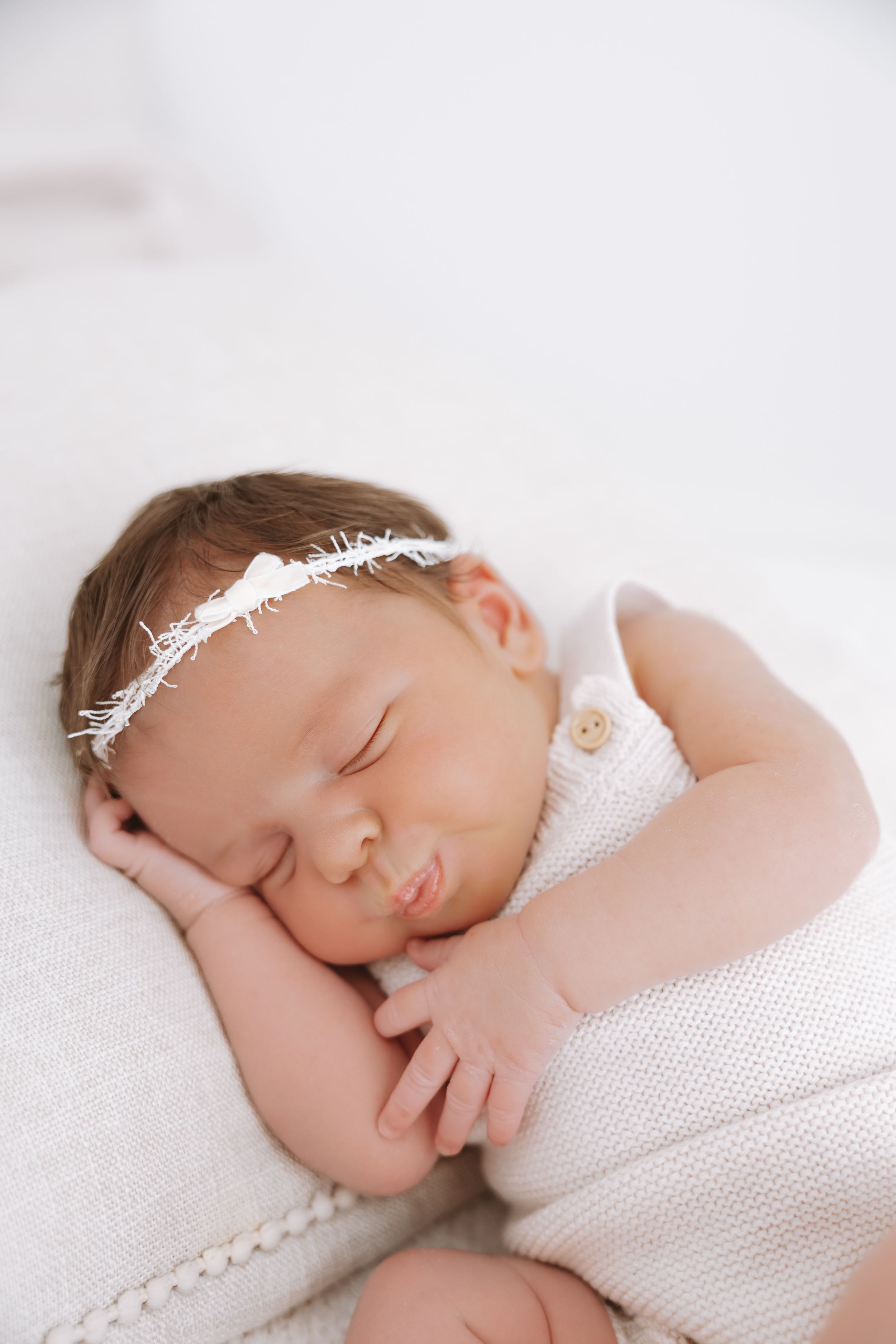 Peaceful newborn baby girl sleeping in white outfit with delicate feather headband on soft blanket.
