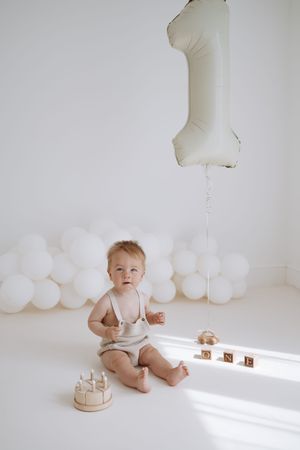 Minimalist white studio scene featuring a baby and white balloons in soft, natural lighting as part of a first birthday setup.