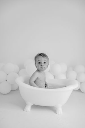 A series of four black and white photos showing baby in a white bathtub surrounded by white balloons.