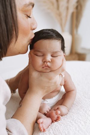 Sweet tender moment between parent and sleeping baby with gentle cheek squishing in soft natural lighting.