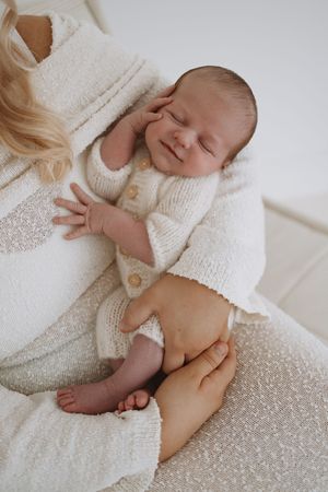 A peacefully sleeping newborn wearing a soft white cardigan rests on cozy knit fabric in natural light.
