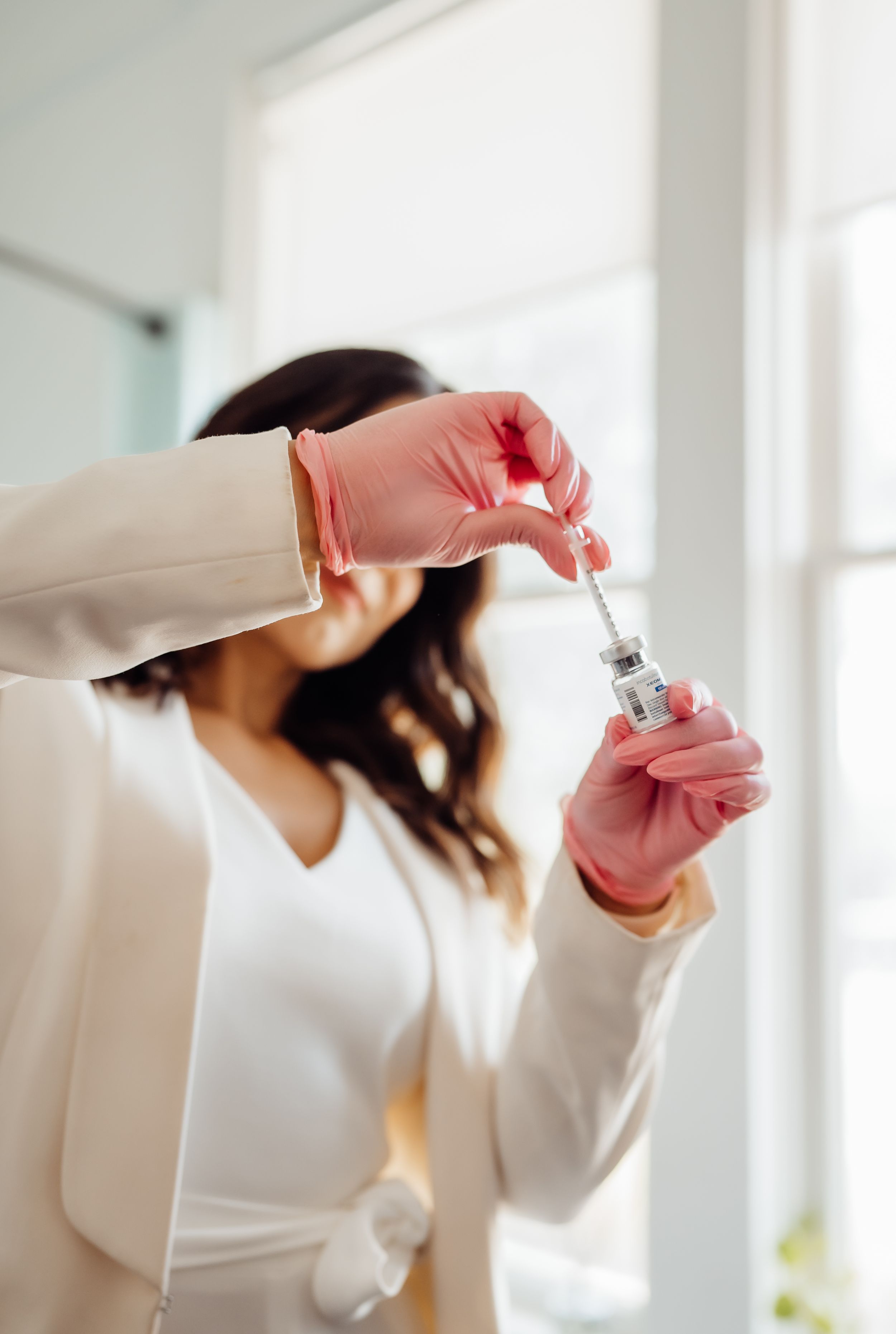 Person in white jacket holding and examining a clear glass bottle.