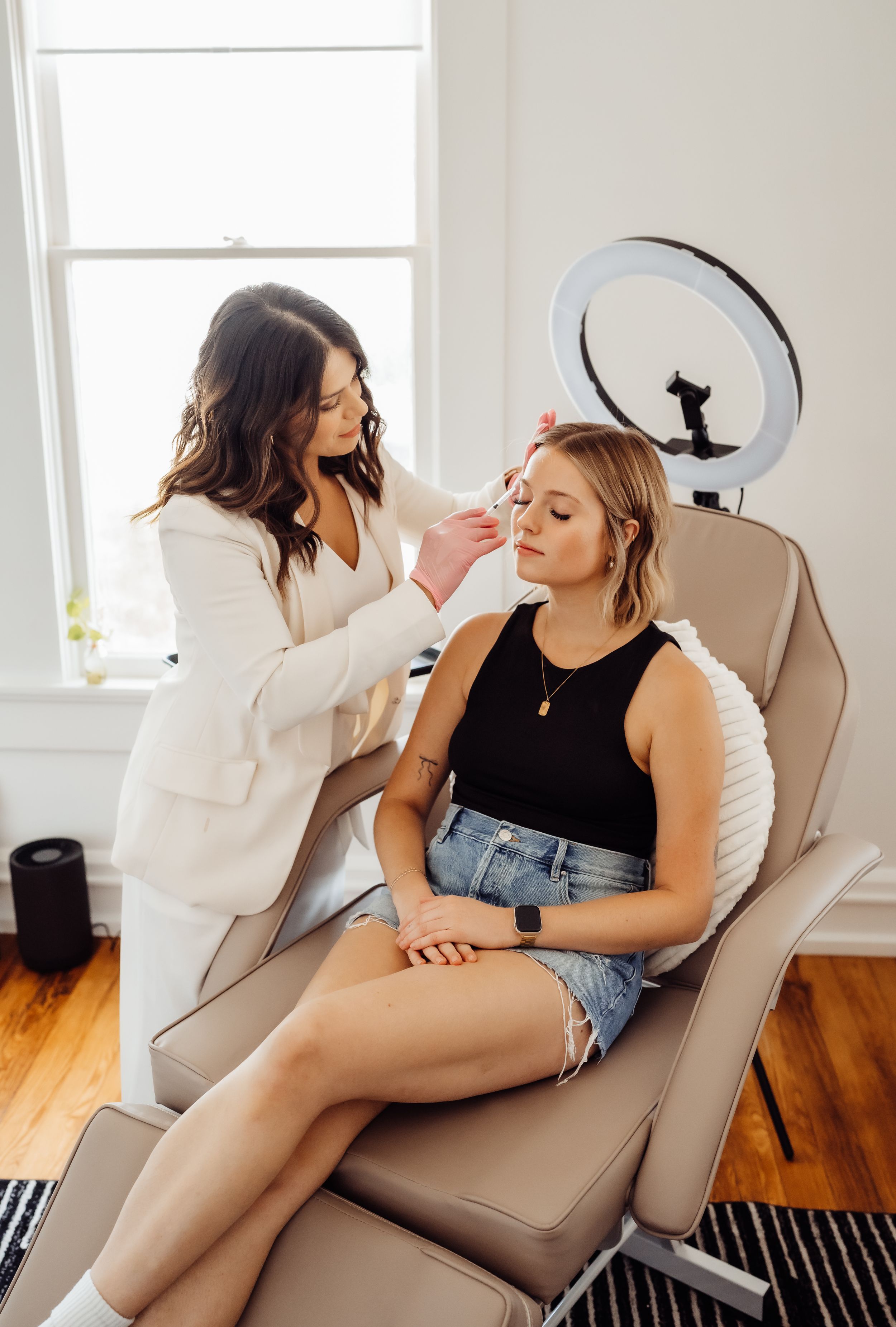 Professional aesthetician applying skincare treatment to client in spa chair.