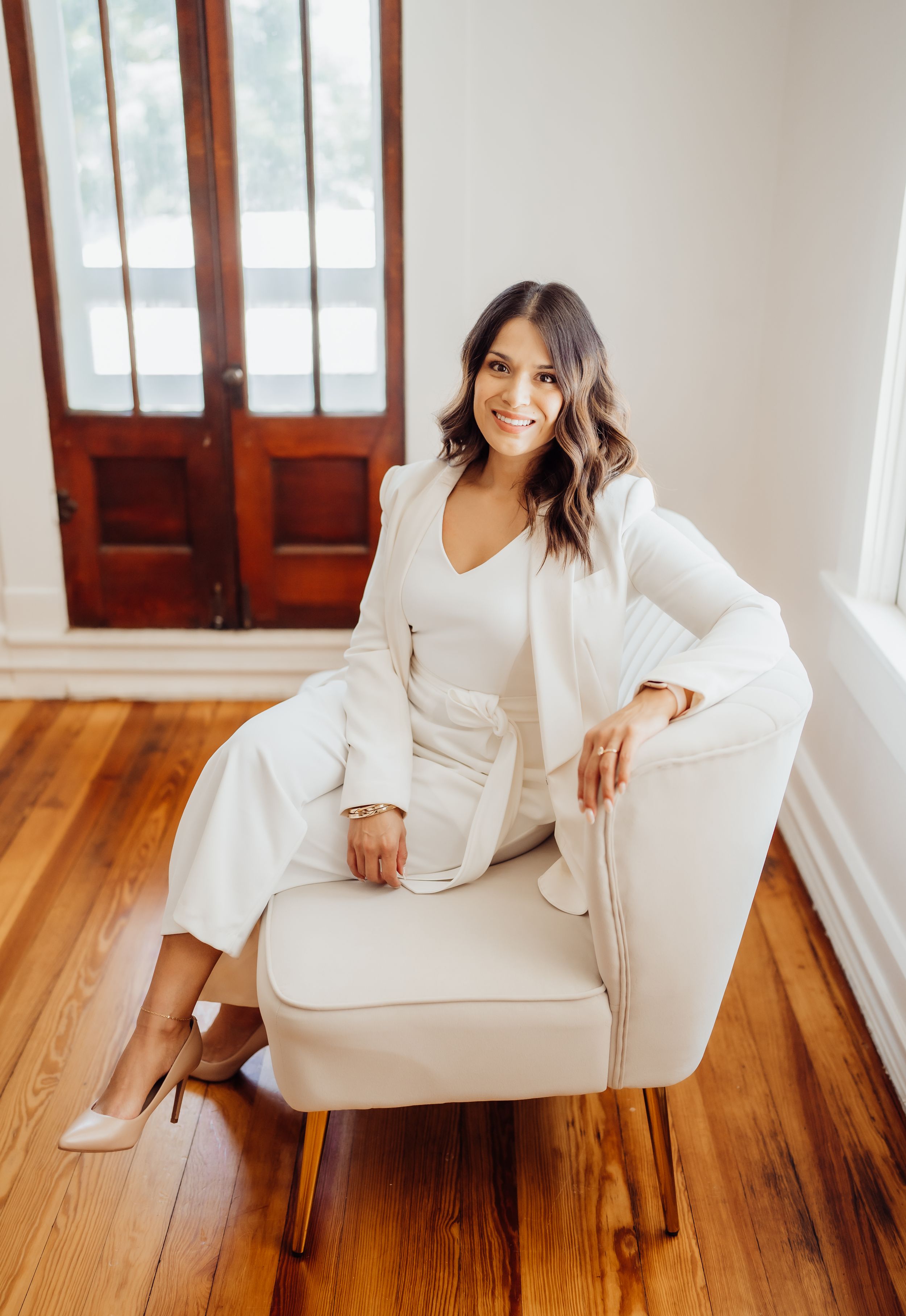 Lifestyle portrait showcasing elegant white business attire while seated in modern accent chair.